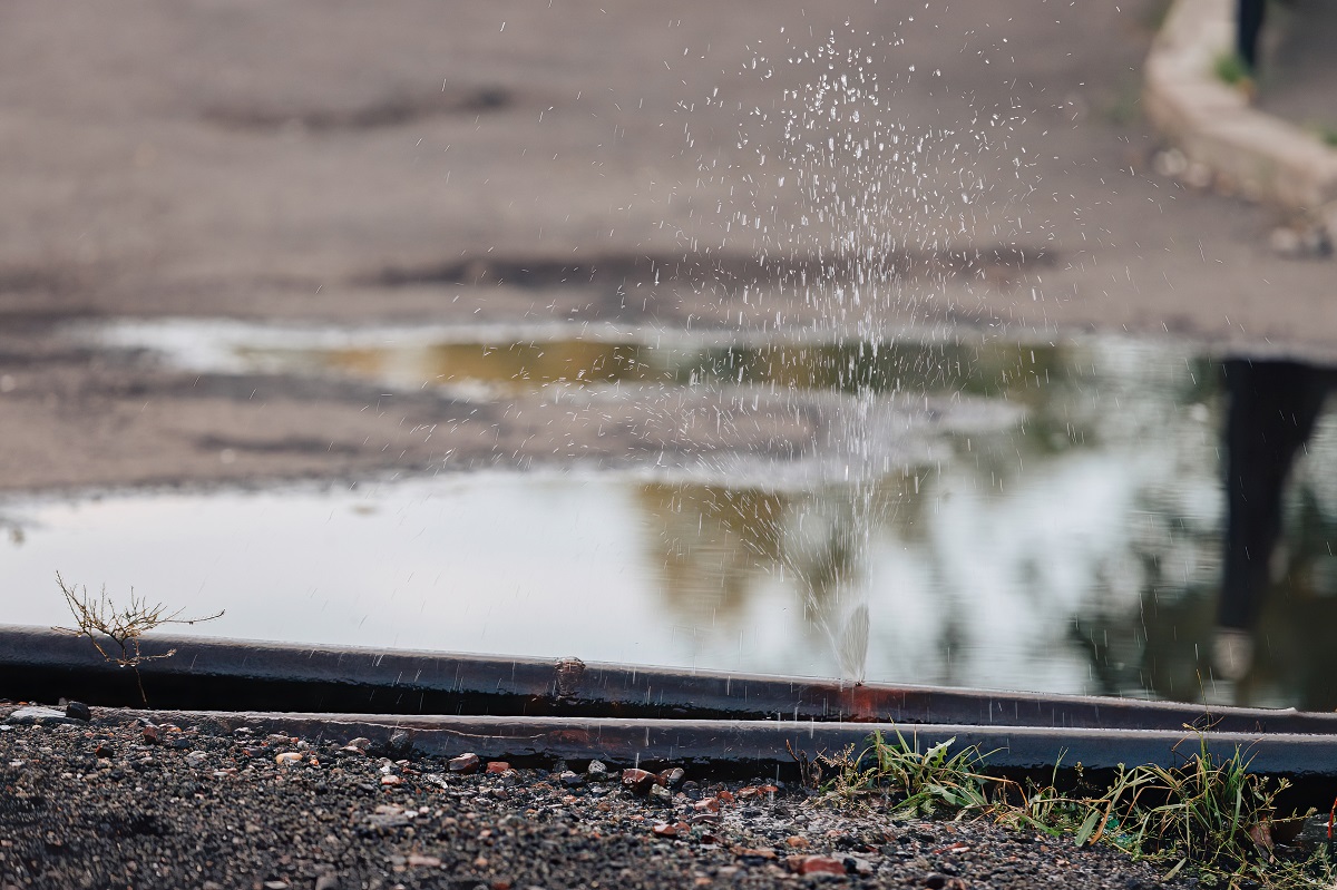 Water splashes from a hole in a metal water pipe.