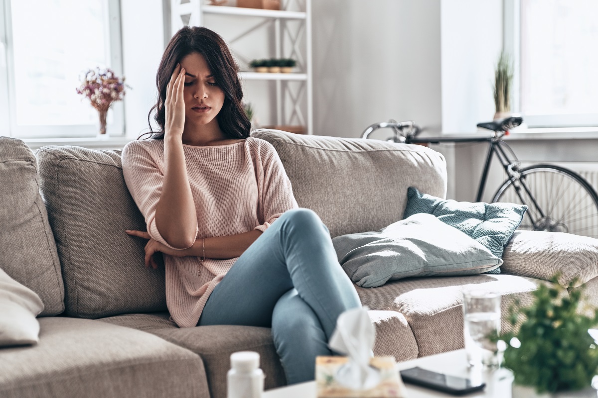 In bad condition. Frustrated young woman suffering from the headache while sitting on the sofa at home