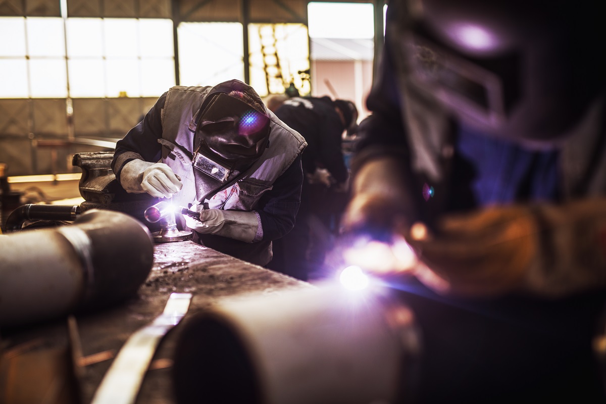 Close up of a male fabric worker cutting metal pipe with an electric grinder in workshop.