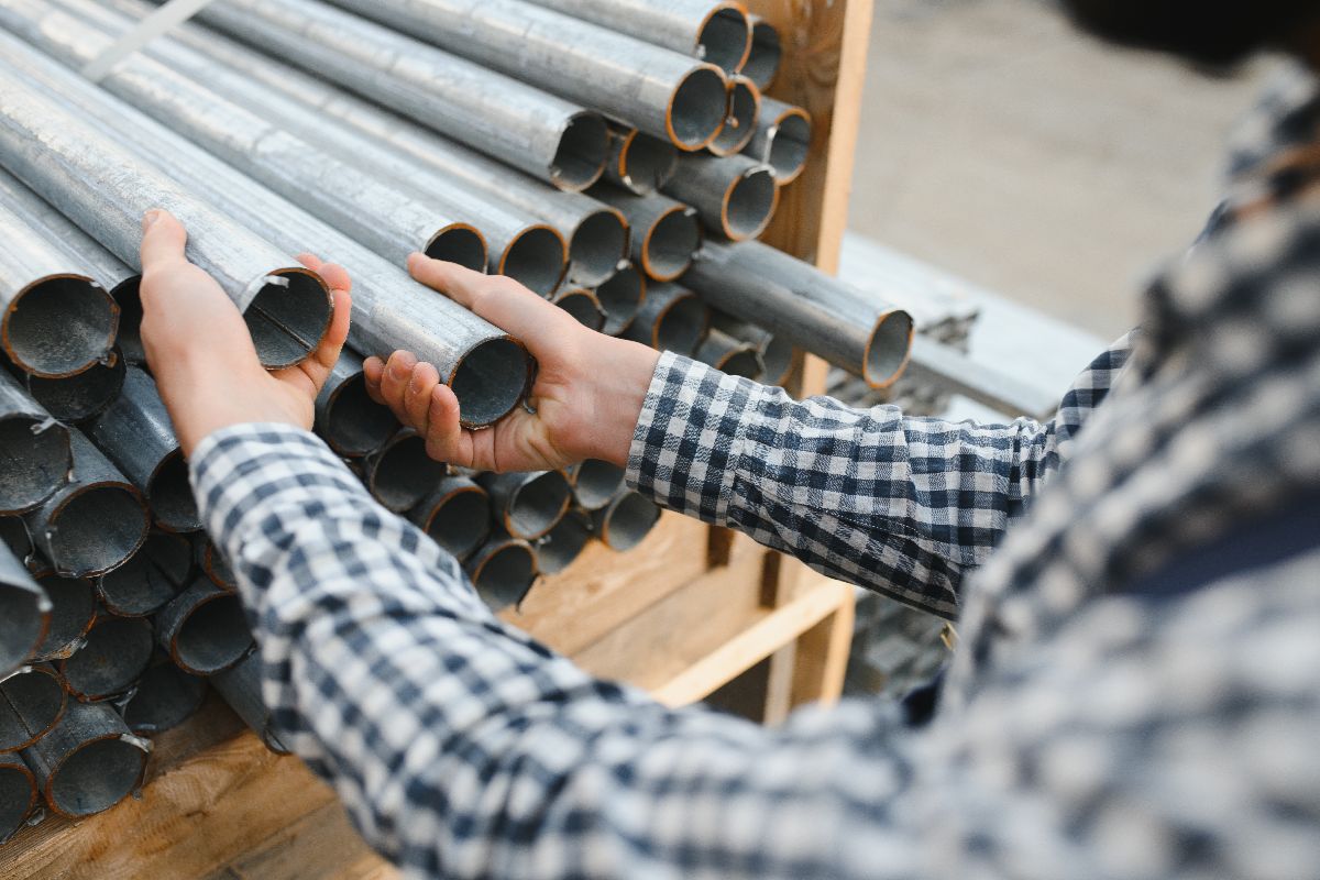 Worker inspecting stacked metal pipes for industrial use