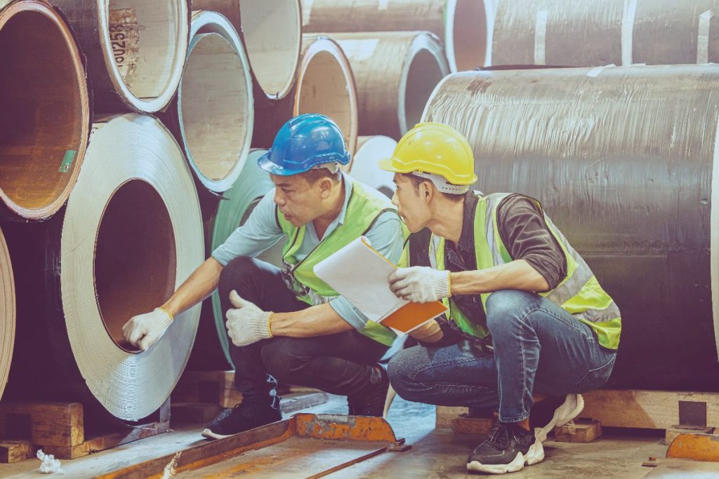 Construction workers inspecting large steel pipes for compliance and quality