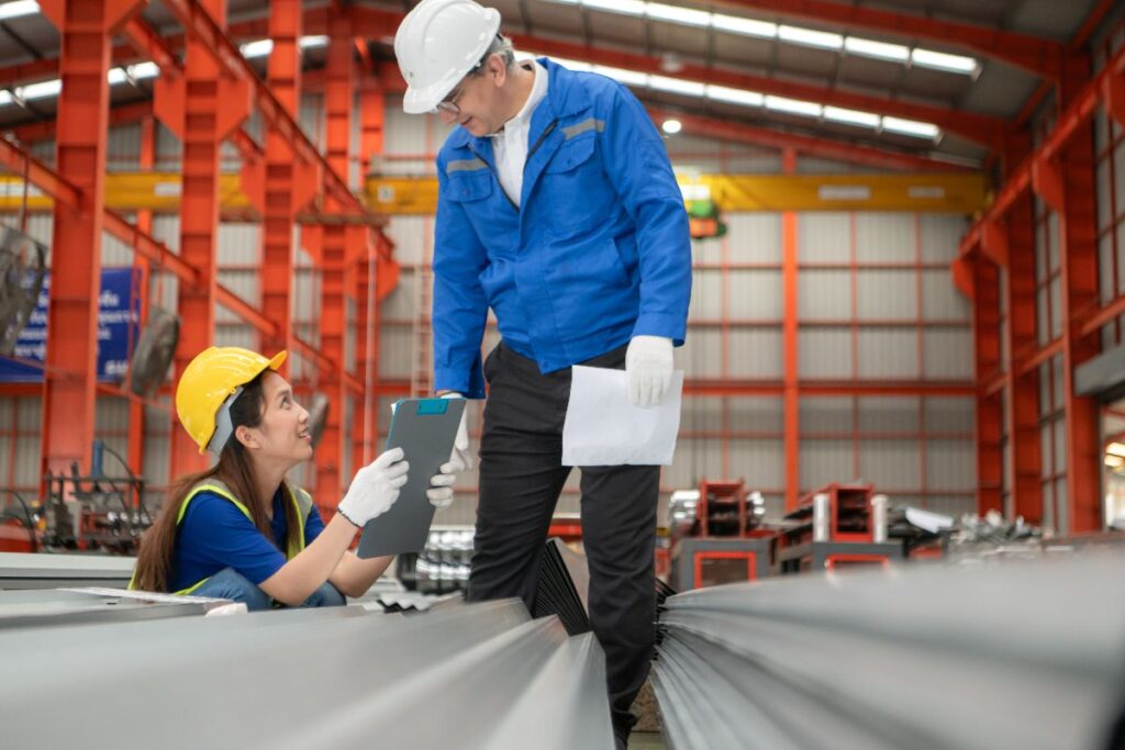 Steel pipe supplier staff inspecting materials and documents inside an industrial warehouse