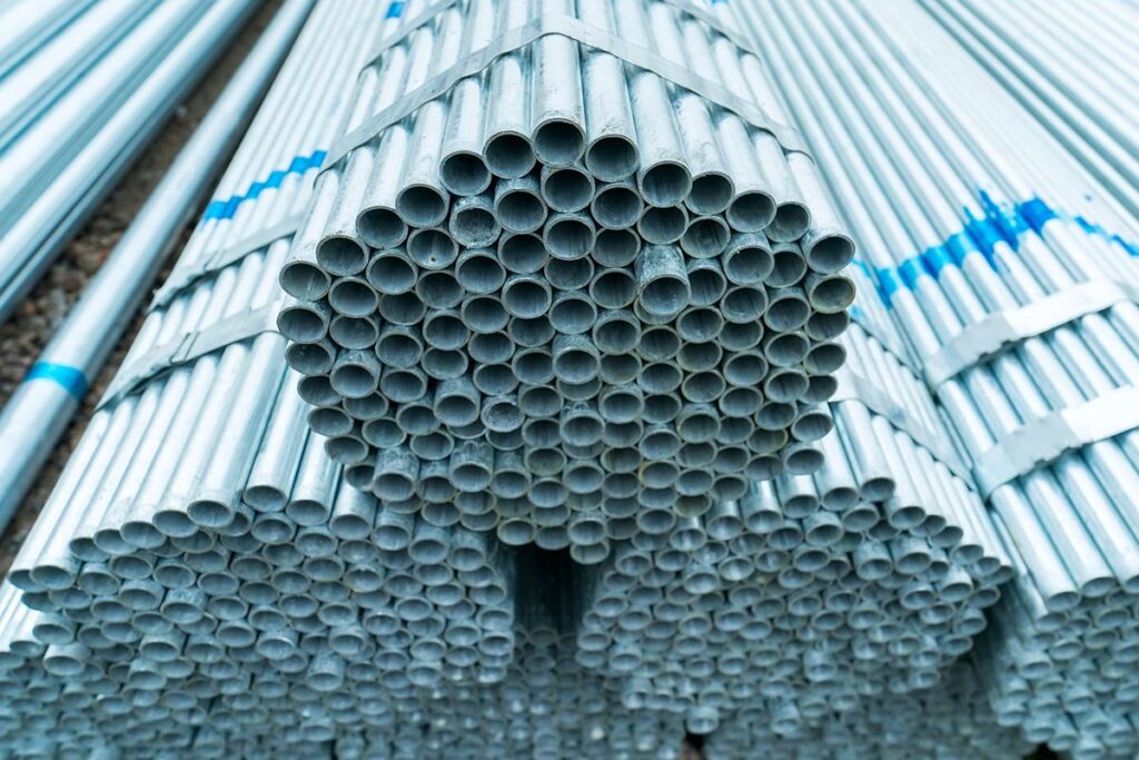 Bundles of galvanized iron pipes stacked in storage, showing their zinc-coated finish and uniform round openings