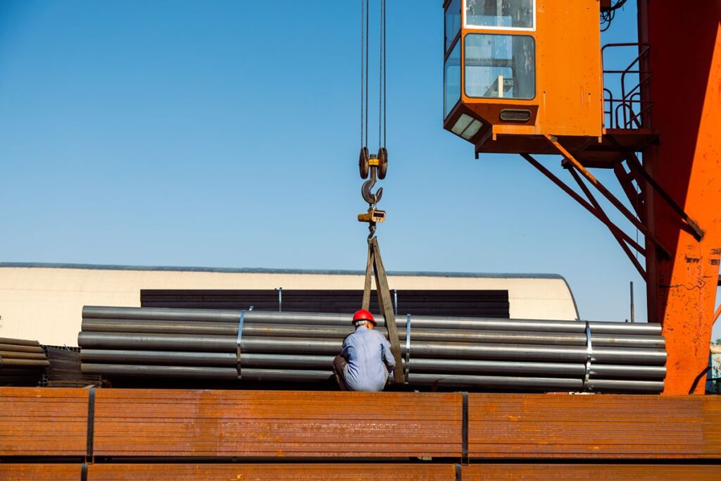 Steel pipes being loaded by crane for transport as part of construction material supply operations