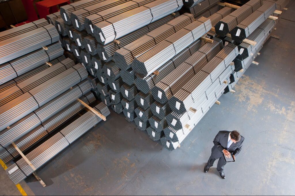 Bundled steel sections stored in a warehouse while a project professional reviews material requirements.