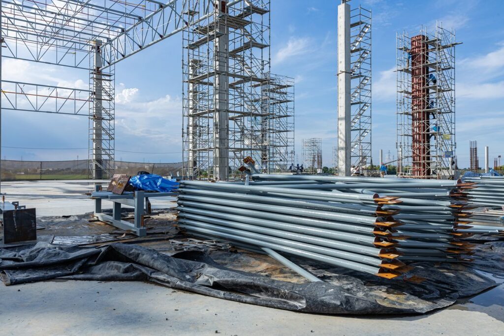 Heavy gauge steel pipes stacked at an active construction site with structural framing in the background