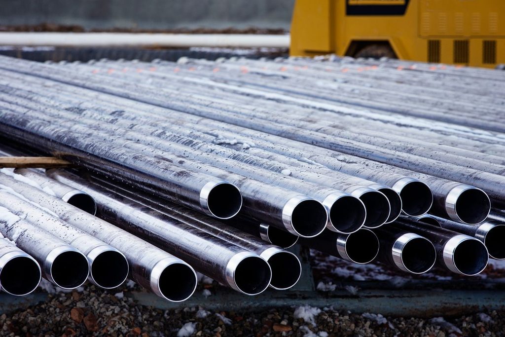 Steel pipes staged at a wet job site, highlighting slippery surfaces and material handling risks during rainy conditions